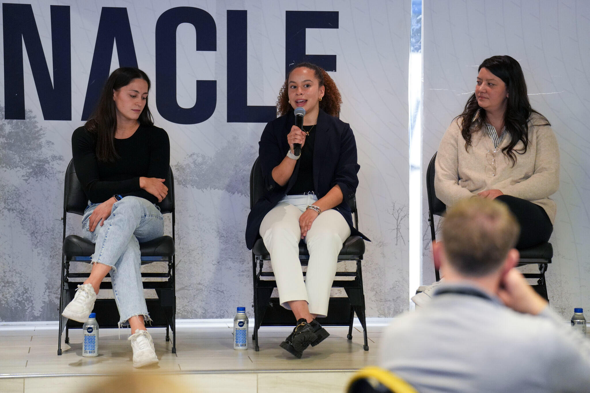 Avril Silva pictured speaking on a panel wearing a blue blazer, white pants and a black shirt